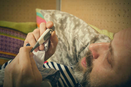 Mature sick man checking body temperature with thermometerの写真素材