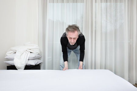 Older man working in bedroom on making bedの写真素材