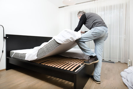 Older man working in bedroom on making bedの写真素材