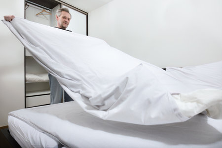 Older man working in bedroom on making bedの写真素材