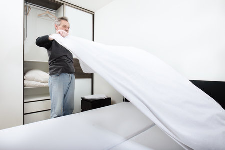Older man working in bedroom on making bedの写真素材