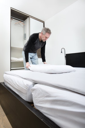 Older man working in bedroom on making bedの写真素材