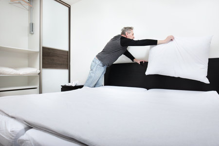 Older man working in bedroom on making bedの写真素材