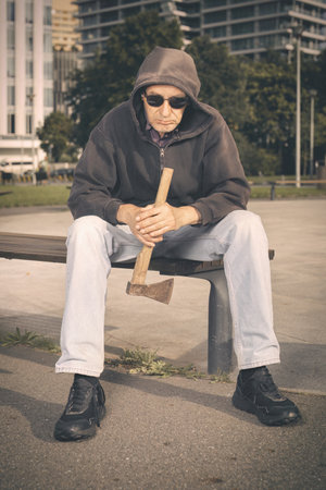 Aggressive older man with ax under the influence of drugs in parkの写真素材