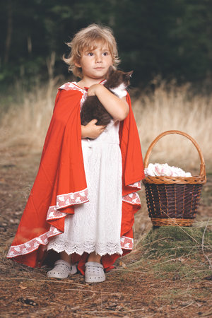 Little red riding hood with basket of food posing with kitten in forestの写真素材