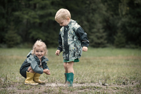 Kids playing on meadow in raincoats after rainingの写真素材