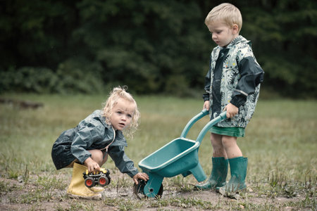 Kids playing on meadow in raincoats after rainingの写真素材