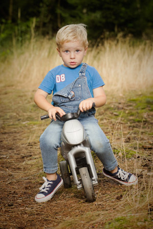 Small boy dressed in jeans posing with bike on footpath in forestの写真素材