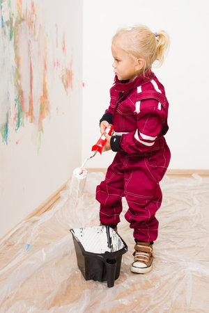 Little blonde girl in overalls repairing and painting white wallの写真素材