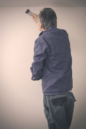 Older man repairing walls and ceiling in empty apartmentの写真素材