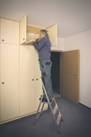 Older man disassembles cabinet in empty apartment ready for paintingの写真素材