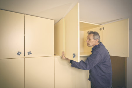 Older man disassembles cabinet in empty apartment ready for paintingの写真素材