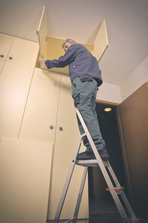Older man disassembles cabinet in empty apartment ready for paintingの写真素材