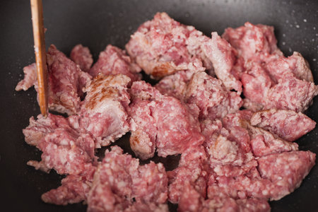 Older man in kitchen frying meat on pan for spaghetti recipeの写真素材