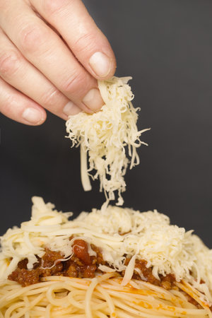 Older man in kitchen grating cheese for spaghetti with minced meat, tomatoes and goudaの写真素材