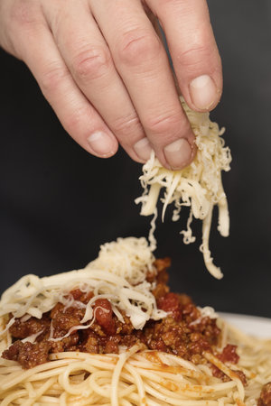 Older man in kitchen grating cheese for spaghetti with minced meat, tomatoes and goudaの写真素材