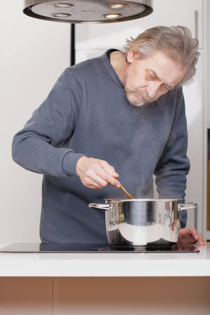 Older man in kitchen boiling spaghetti for classic recipeの写真素材