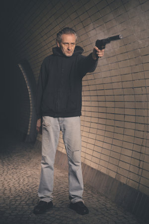 Old member of criminal gang armed with handgun shooting in gun smokeの写真素材