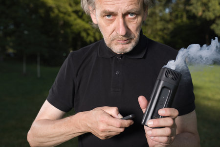 Older man uses two types of smoke machine generators on outdoor locationの写真素材