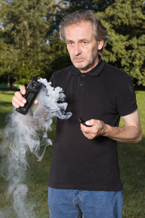 Older man uses two types of smoke machine generators on outdoor locationの写真素材