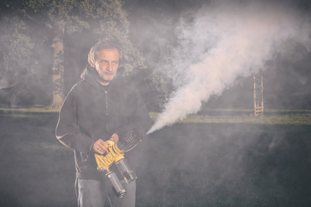 Older man uses two types of smoke machine generators on outdoor locationの写真素材