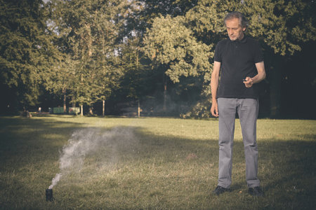 Older man uses two types of smoke machine generators on outdoor locationの写真素材