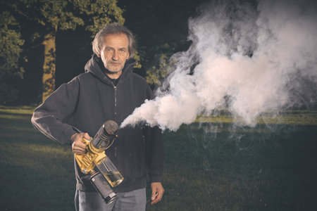 Older man uses two types of smoke machine generators on outdoor locationの写真素材