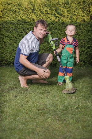 Little boy with father playing with power and garden tools on garden lawnの写真素材
