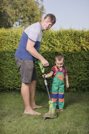 Little boy with father playing with power and garden tools on garden lawn