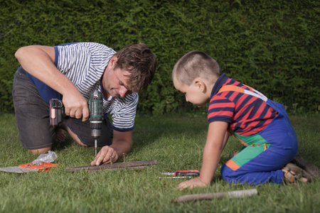 Little boy with father playing with power and garden tools on garden lawnの写真素材