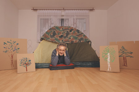 Older man in senior age relaxing in apartment room in tent instead of outdoor campingの写真素材