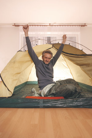 Older man in senior age relaxing in apartment room in tent instead of outdoor campingの写真素材