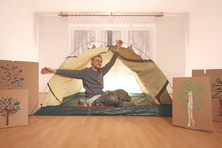 Older man in senior age relaxing in apartment room in tent instead of outdoor campingの写真素材