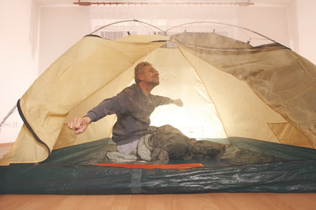 Older man in senior age relaxing in apartment room in tent instead of outdoor campingの写真素材