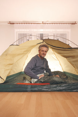 Older man in senior age relaxing in apartment room in tent instead of outdoor campingの写真素材
