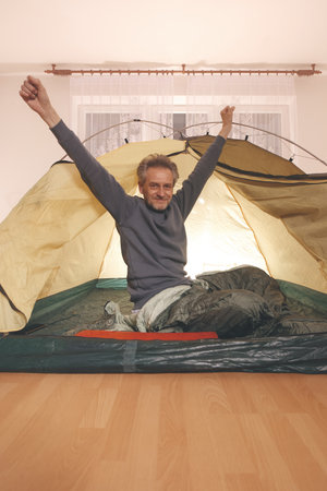 Older man in senior age relaxing in apartment room in tent instead of outdoor campingの写真素材