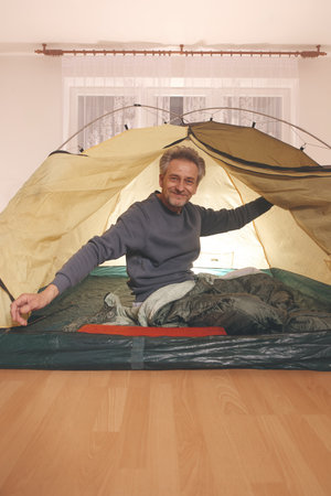 Older man in senior age relaxing in apartment room in tent instead of outdoor campingの写真素材