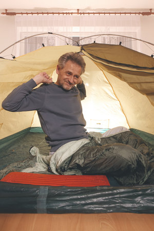 Older man in senior age relaxing in apartment room in tent instead of outdoor campingの写真素材
