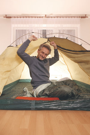 Older man in senior age relaxing in apartment room in tent instead of outdoor campingの写真素材