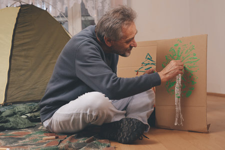 Older man in senior age relaxing in apartment room in tent instead of outdoor campingの写真素材