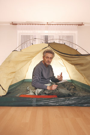 Older man in senior age relaxing in apartment room in tent instead of outdoor campingの写真素材