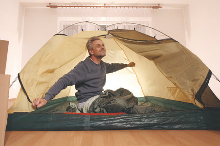 Older man in senior age relaxing in apartment room in tent instead of outdoor campingの写真素材