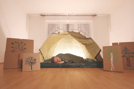 Older man in senior age relaxing in apartment room in tent instead of outdoor campingの写真素材