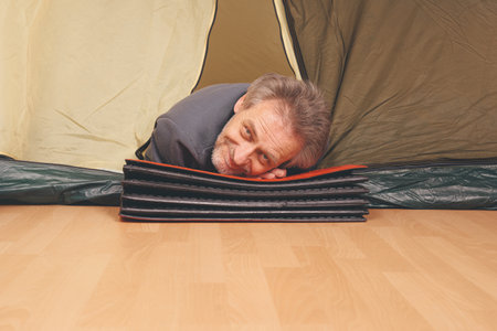 Older man in senior age relaxing in apartment room in tent instead of outdoor campingの写真素材