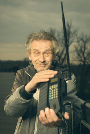 Older man outdoor on bridge using retro cellphoneの写真素材