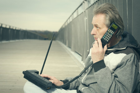 Older man outdoor on bridge using retro cellphone to callの写真素材