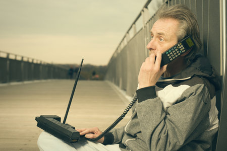 Older man outdoor on bridge using retro cellphone to call