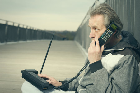 Older man outdoor on bridge using retro cellphone to callの写真素材