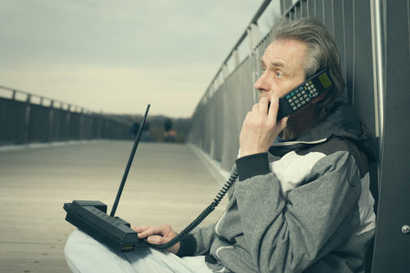 Older man outdoor on bridge using retro cellphone to callの写真素材