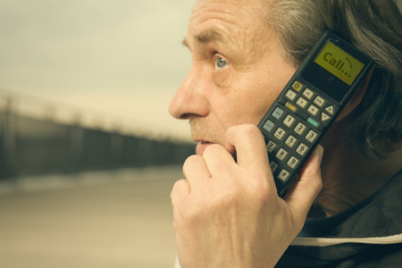 Older man outdoor on bridge using retro cellphone to callの写真素材